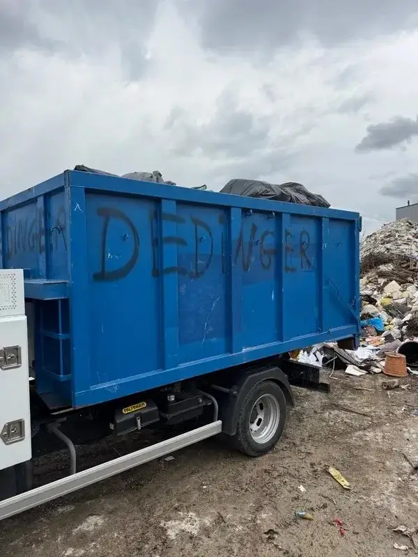 Benne bleue JDM sur son camion, devant un tas de gravats
