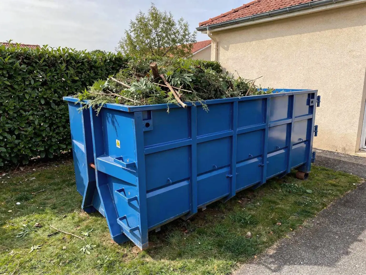 Benne bleue remplie de déchets verts et de branches dans un jardin près de Lyon